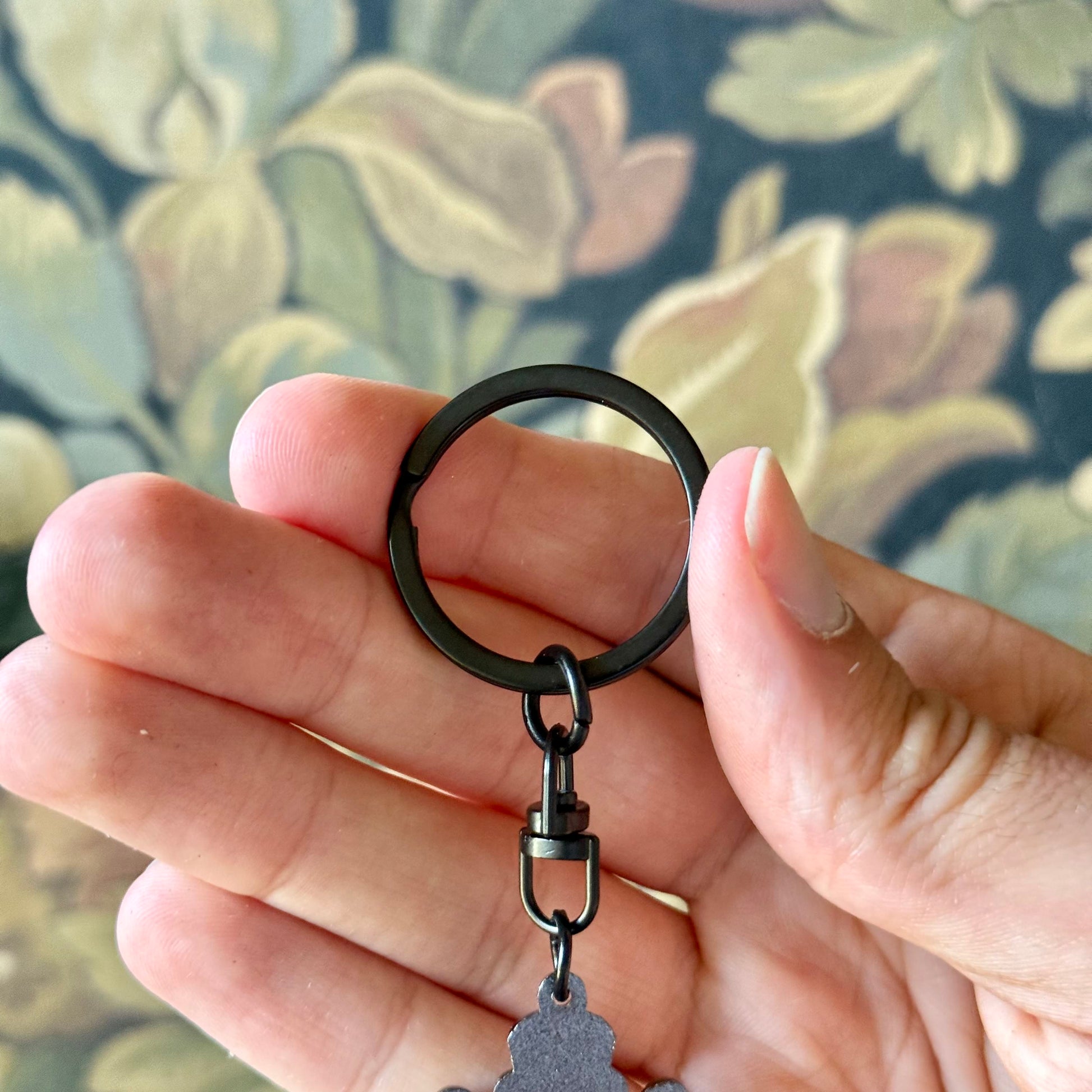 Hand holding a black keychain with a floral patterned background