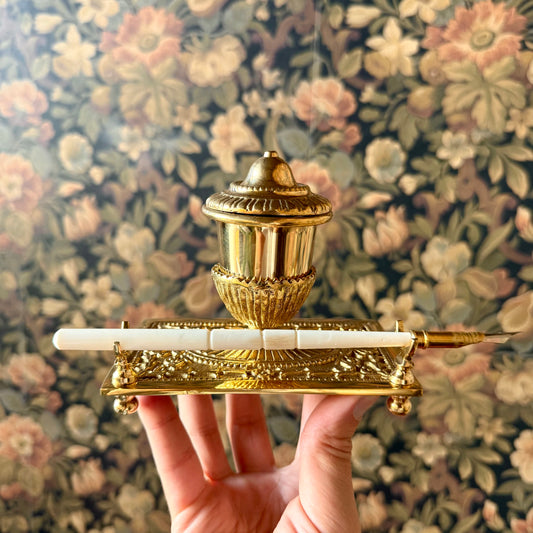 A beautifully crafted Victorian-style brass inkwell set, including an ornate brass inkwell with a hinged lid, a bone nib pen, and a packet of powdered ink, elegantly arranged on a vintage desk.