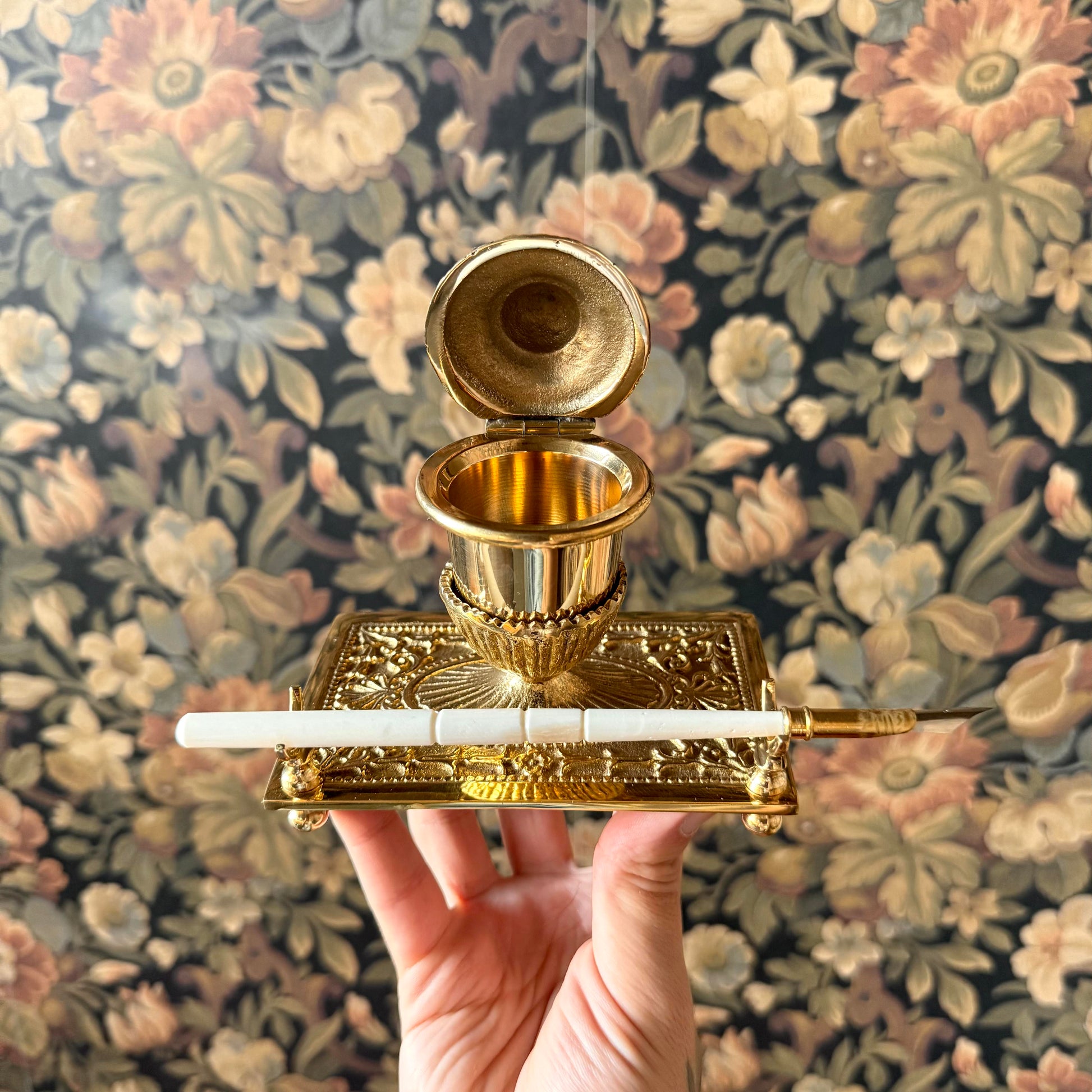 A beautifully crafted Victorian-style brass inkwell set, including an ornate brass inkwell with a hinged lid, a bone nib pen, and a packet of powdered ink, elegantly arranged on a vintage desk.