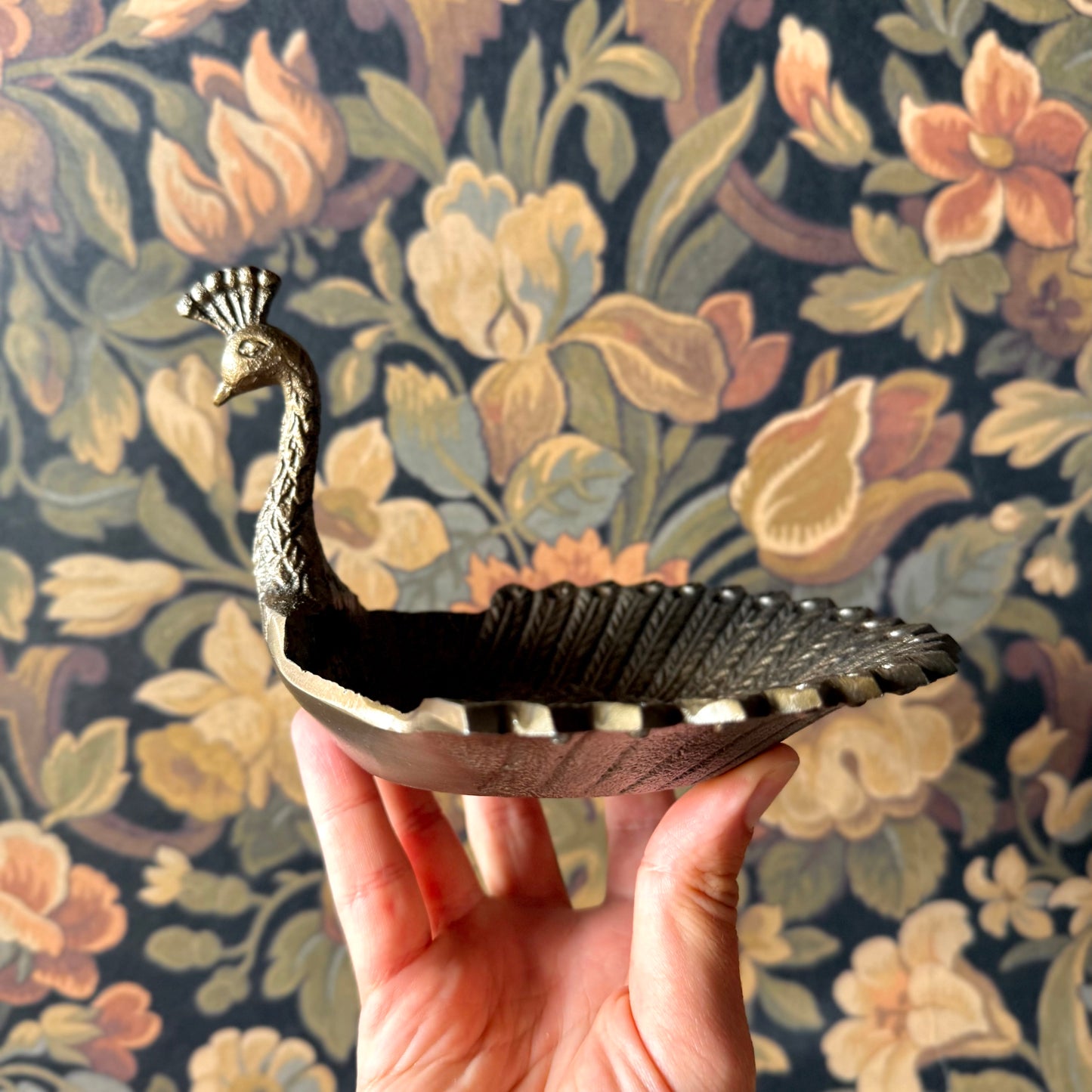 Decorative peacock-shaped dish held in front of a floral-patterned background