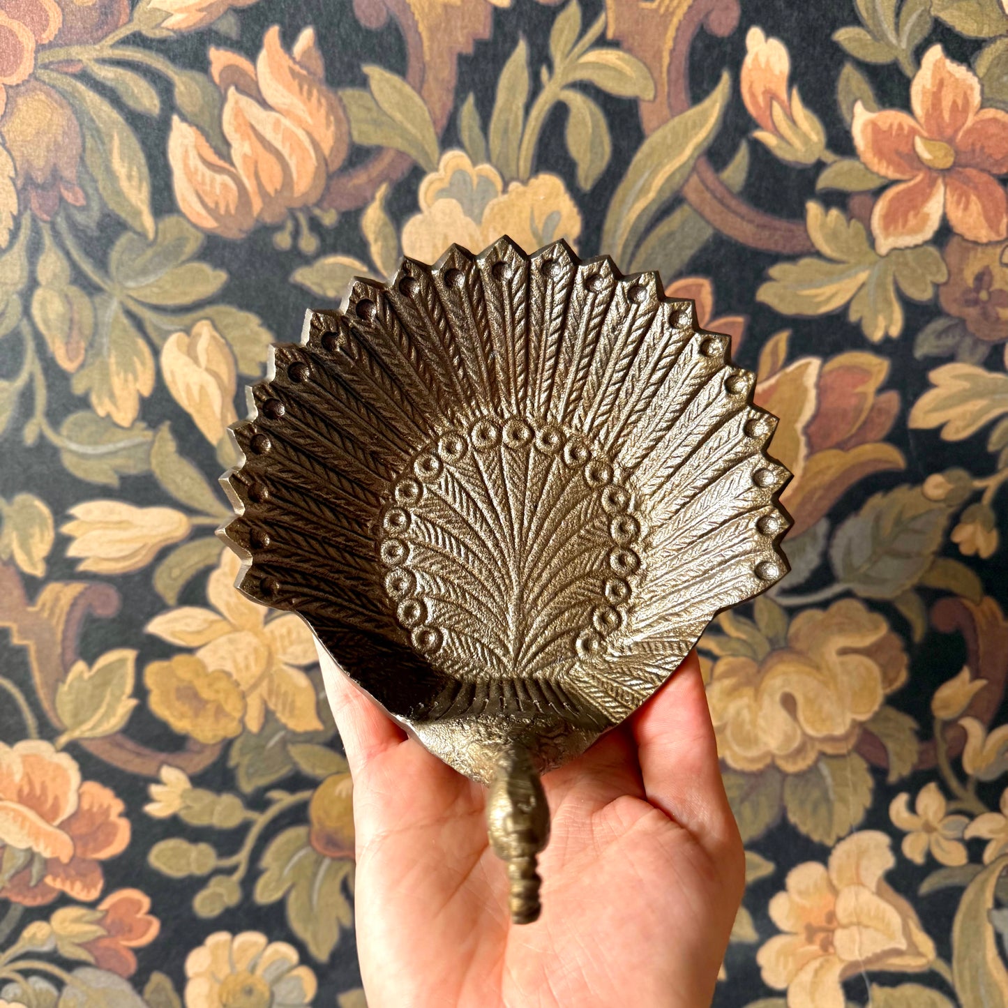 Decorative metal peacock feather held against a floral patterned background