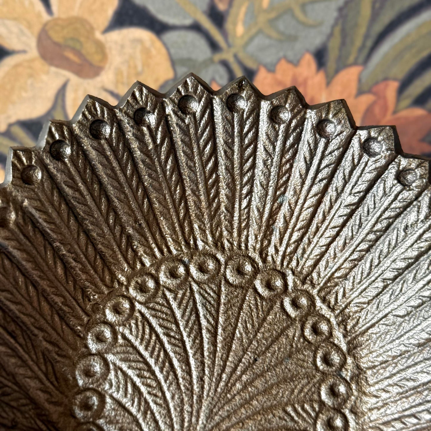 Decorative metal plate with intricate fan-like design on a floral-patterned fabric background