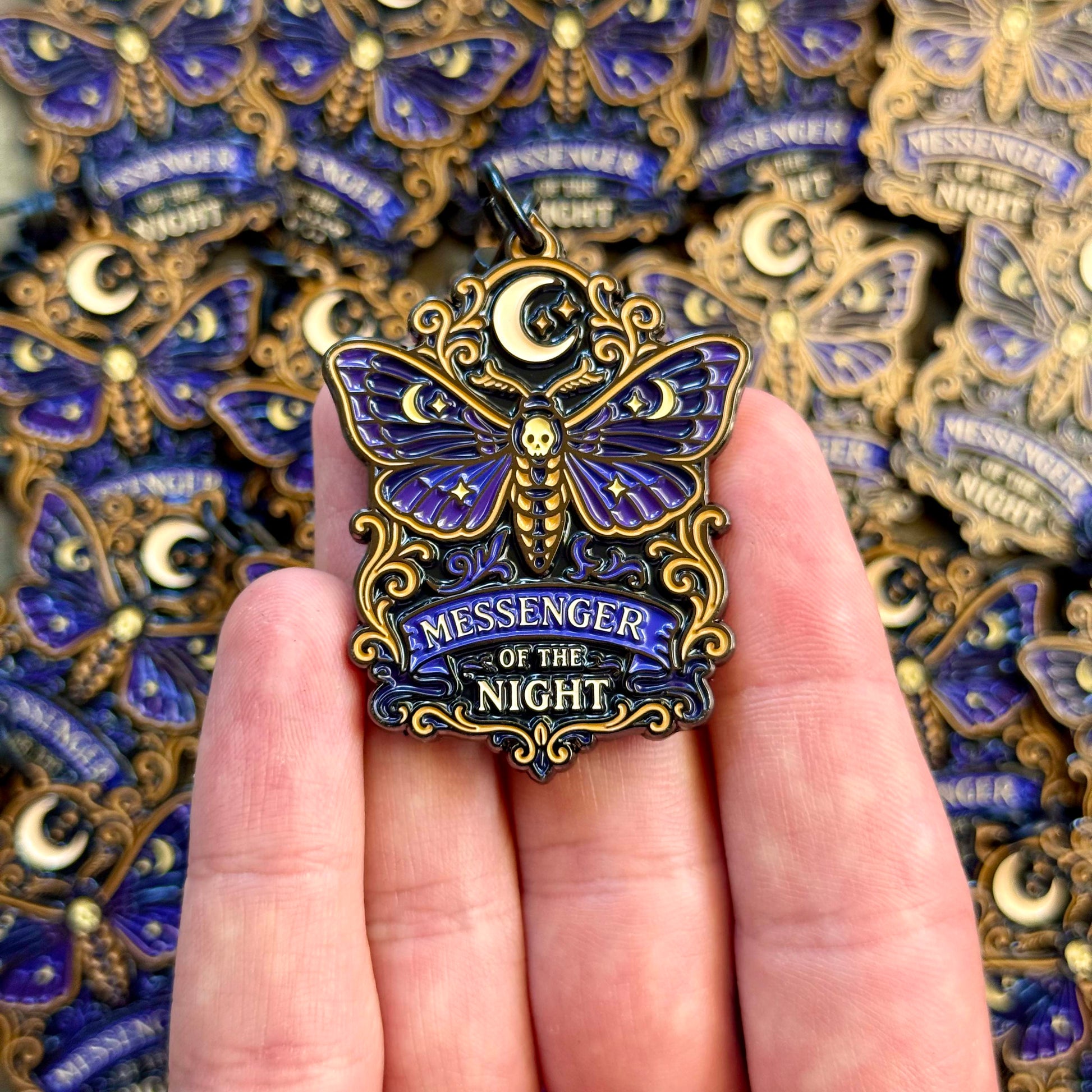 Moth-shaped 'Messenger of the Night' keychain held in a hand with a patterned background.