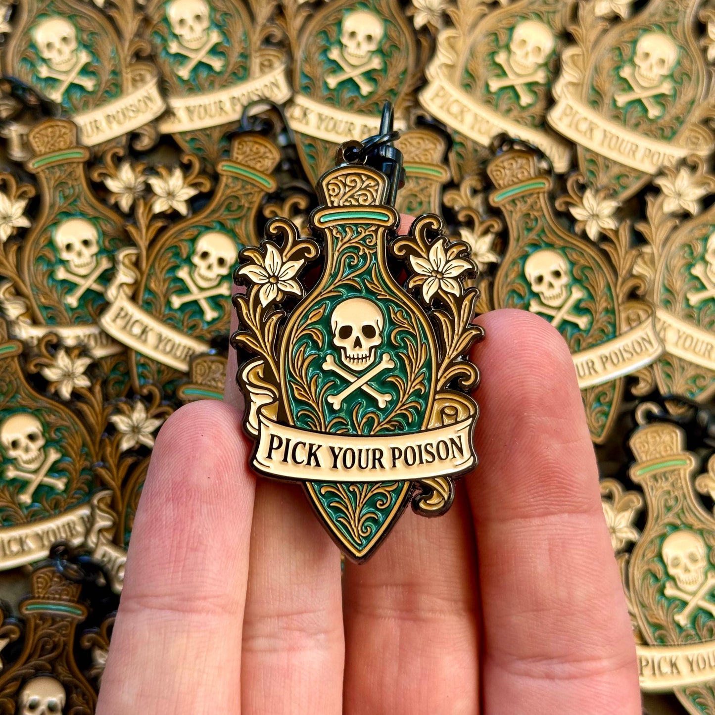 Enamel keychain with 'Pick Your Poison' design held in a hand, with multiple keychains in the background.