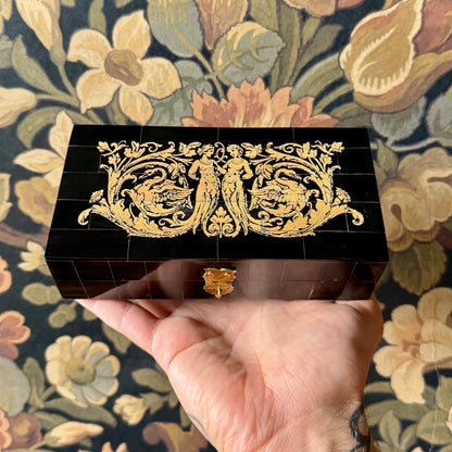 A rectangular black horn box with a mosaic tile exterior made from real water buffalo horn. The box features a brass latch and is displayed closed on a neutral background.