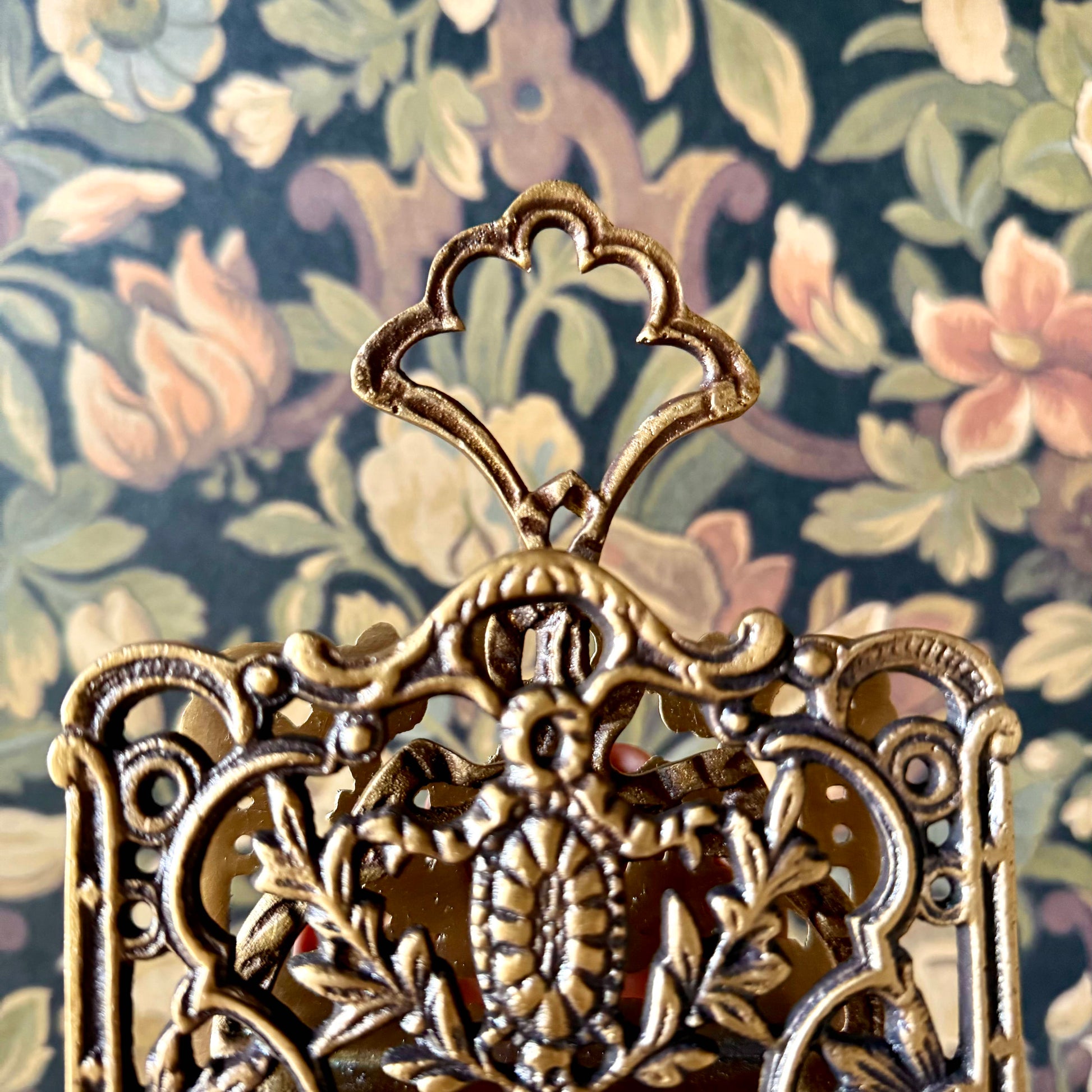 A detailed close-up of the Antique Brass Napkin and Letter Holder, showing its ornate curves and aged brass patina on a lace tablecloth.