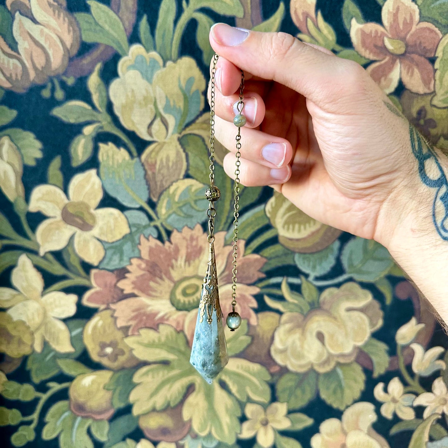 Victorian-inspired labradorite pendulum with exquisite brass detailing. The labradorite stone, known for its shimmering play of colors, is suspended from a brass chain, perfect for both divination and as a striking decorative accent.