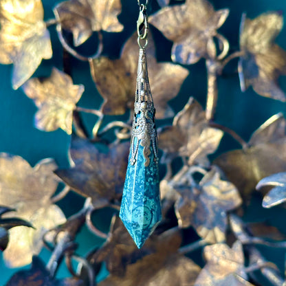 Victorian-inspired malachite pendulum featuring detailed brass accents. The malachite stone, with its rich green hues and natural banding, is suspended from a brass chain, ideal for spiritual practices or vintage-style decor.