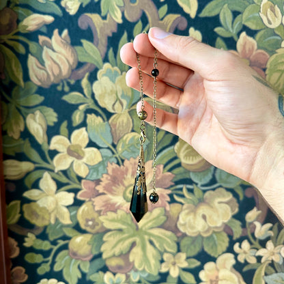 Victorian-inspired obsidian pendulum adorned with brass detailing. The deep black obsidian stone is polished to a smooth finish and hangs from a brass chain, suitable for dowsing or as an elegant decorative item.