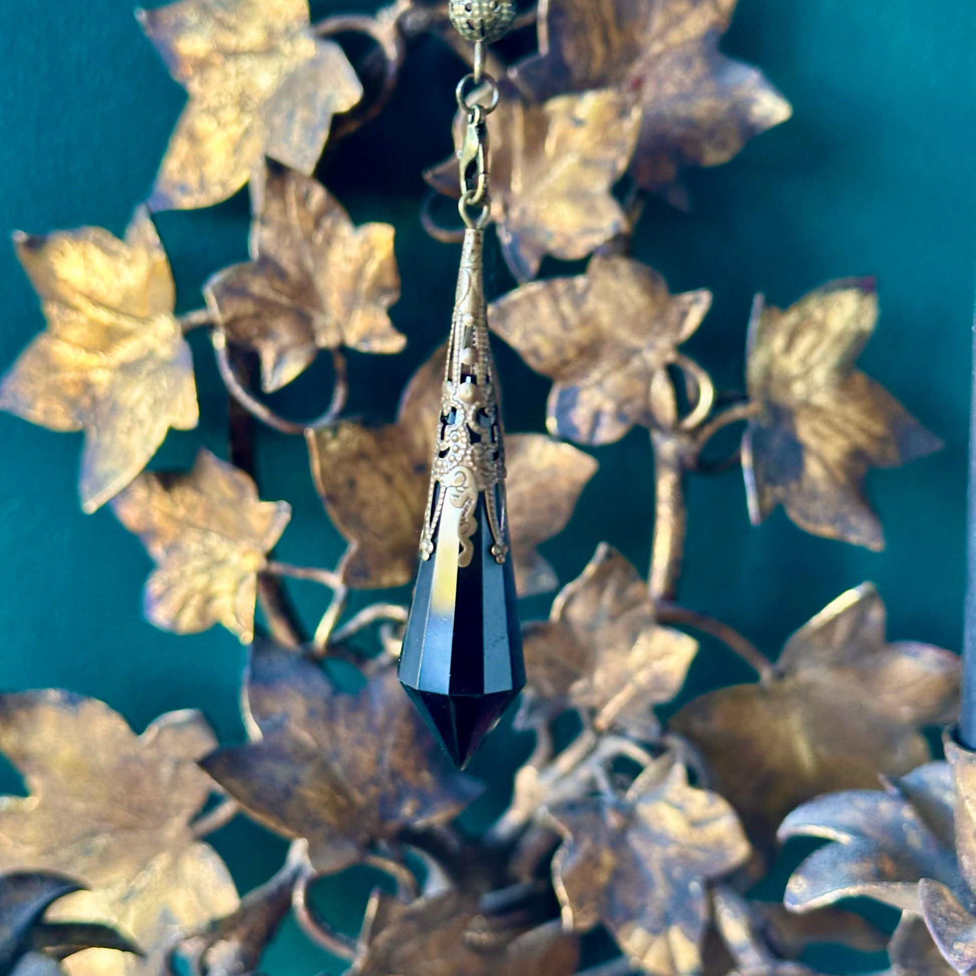 Victorian-inspired obsidian pendulum adorned with brass detailing. The deep black obsidian stone is polished to a smooth finish and hangs from a brass chain, suitable for dowsing or as an elegant decorative item.