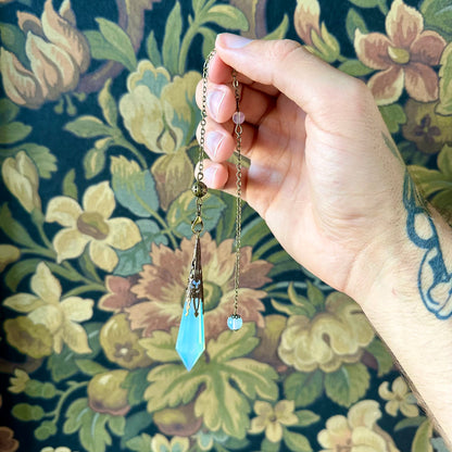 Victorian-inspired opalite pendulum with intricate brass detailing. The opalite stone, known for its ethereal, milky appearance, hangs gracefully from a brass chain, perfect for divination or as a decorative piece.