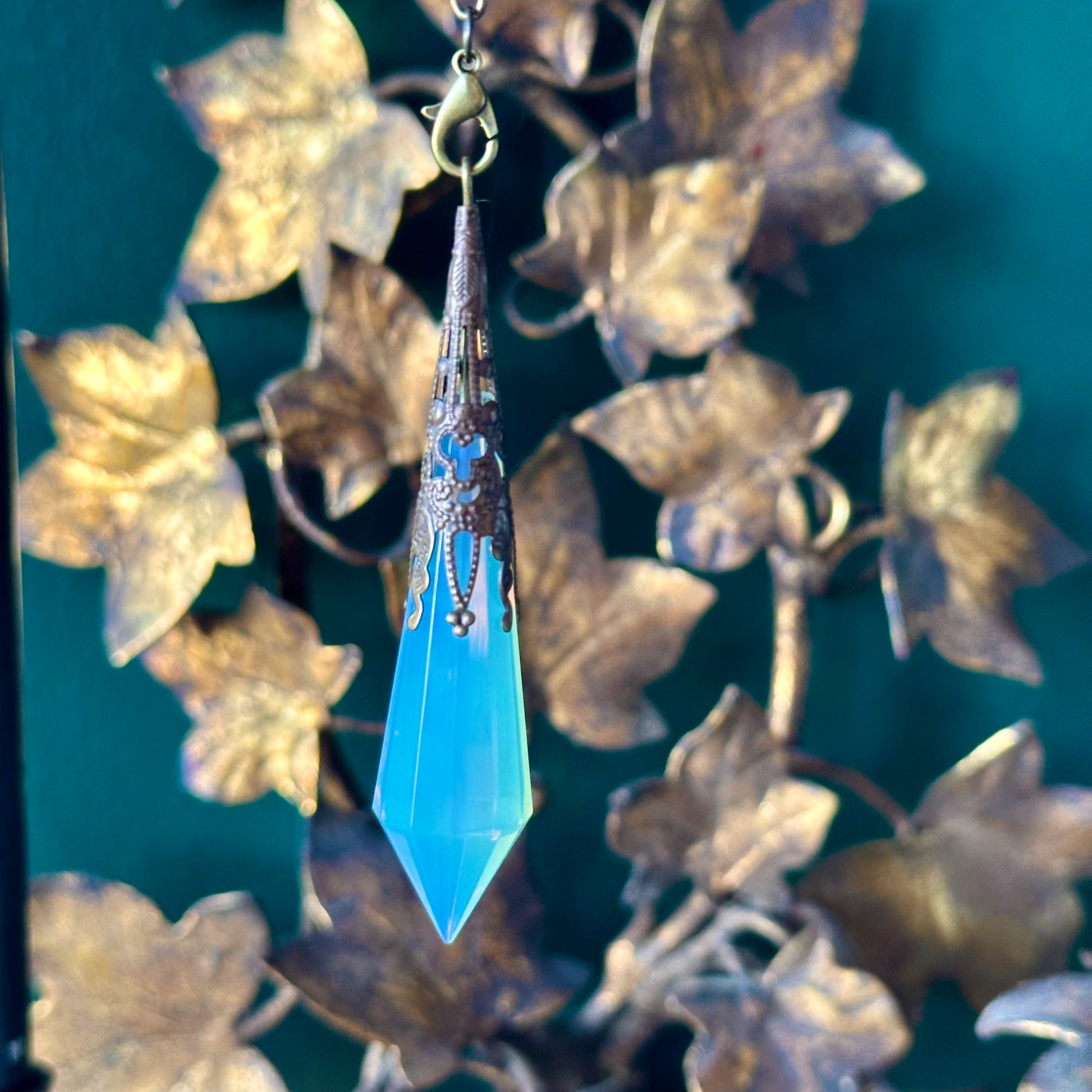 Victorian-inspired opalite pendulum with intricate brass detailing. The opalite stone, known for its ethereal, milky appearance, hangs gracefully from a brass chain, perfect for divination or as a decorative piece.