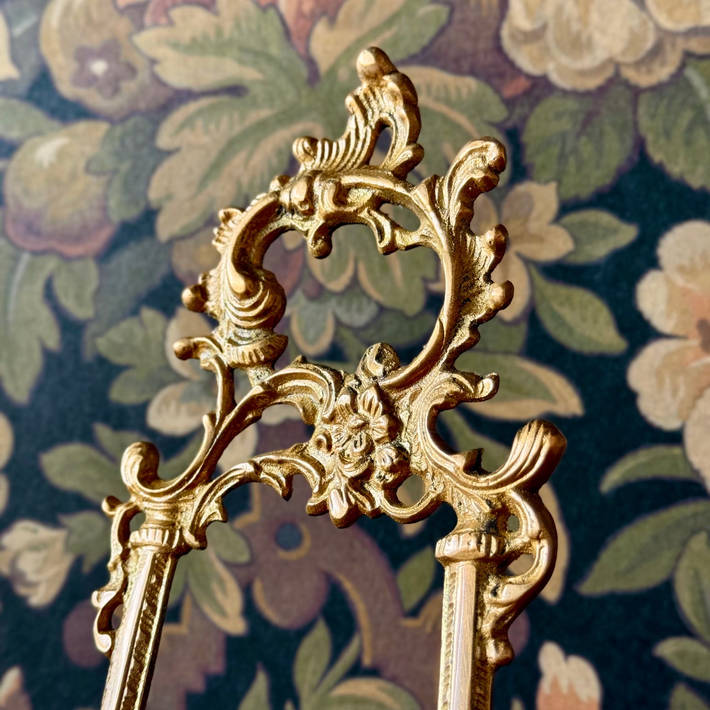Close-up of the top of the brass easel, highlighting the intricate floral motif and aged patina of the metal surface.
