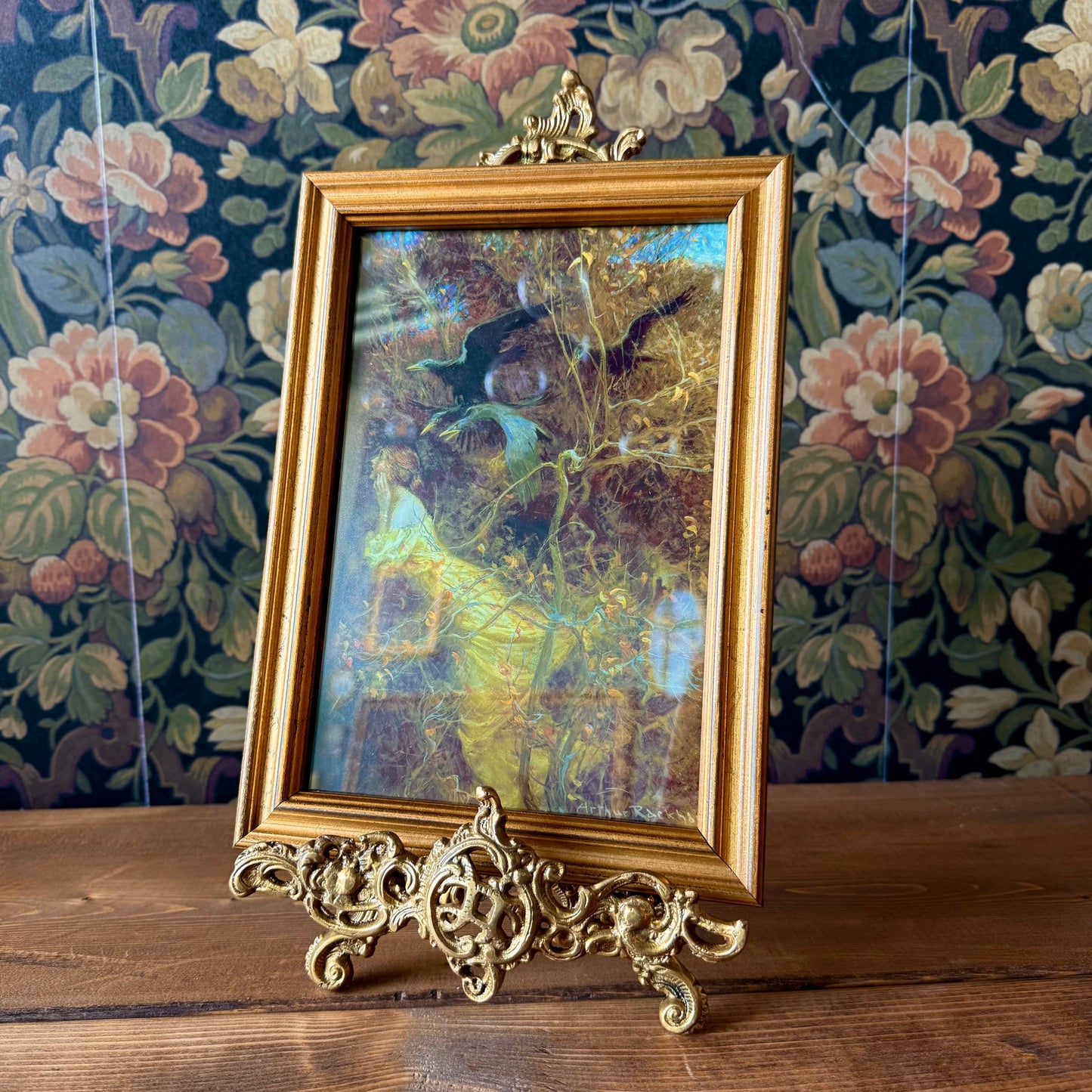 Side profile of the antiqued brass easel showing its folding back leg and three-dimensional scroll accents in a vintage finish.