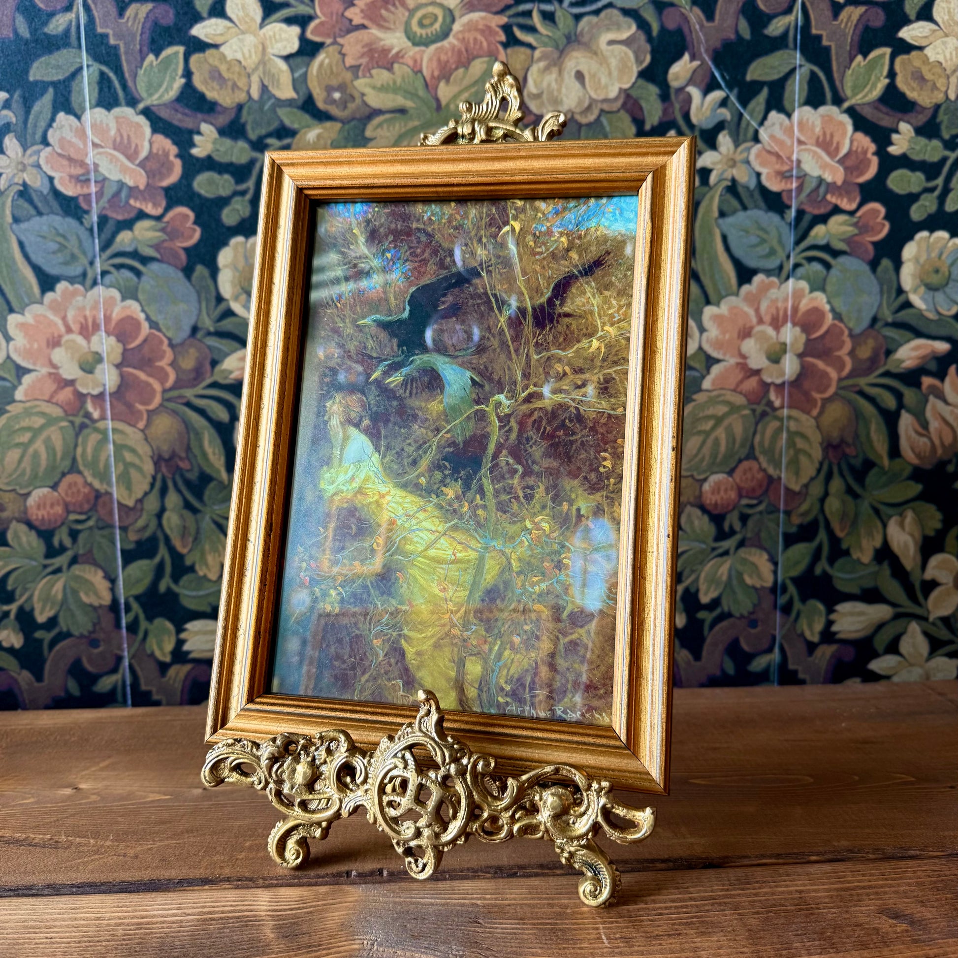 Side profile of the antiqued brass easel showing its folding back leg and three-dimensional scroll accents in a vintage finish.