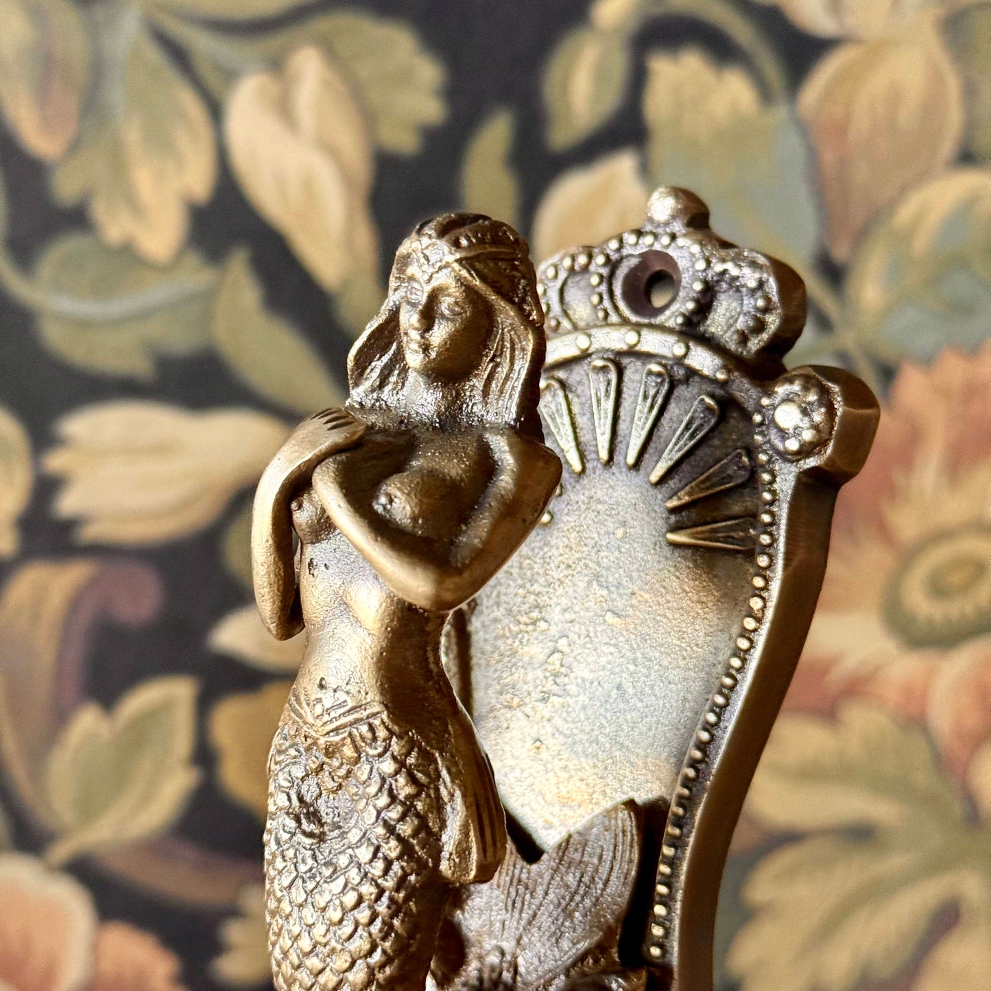 Antiqued brass coat hanger featuring a detailed mermaid figure with flowing hair and etched design, mounted on a neutral background. The vintage-style hook is solid and sculptural, measuring 5 inches in length.