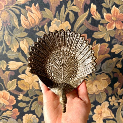 Decorative metal peacock feather held against a floral patterned background