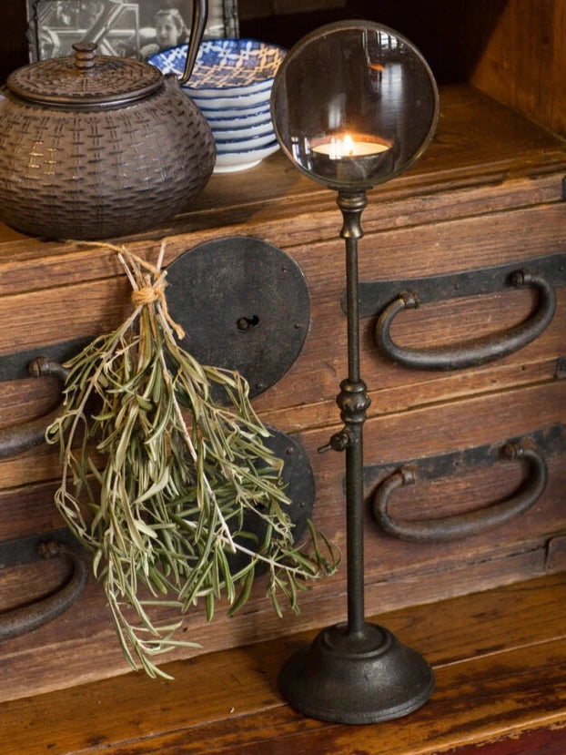 Decorative candle holder with a teapot and dried plants on a wooden surface