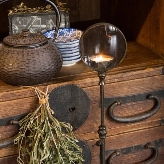 Decorative candle holder with a teapot and dried plants on a wooden surface