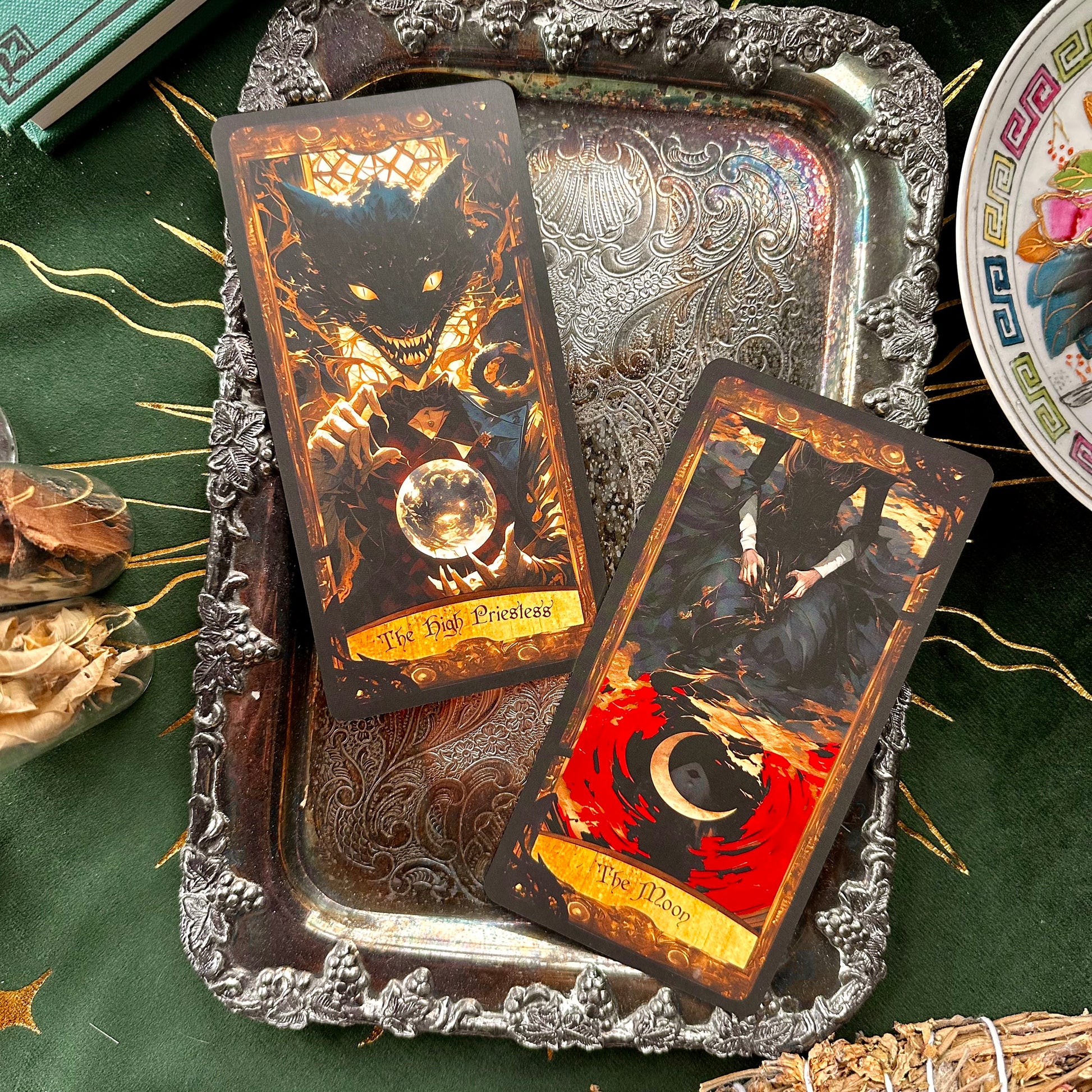 Two tarot cards shown side-by-side; one features the ethereal Moon with dreamy, mysterious imagery, while the High Priestess card depicts the grinning Cheshire Cat, symbolizing hidden knowledge and intuition.