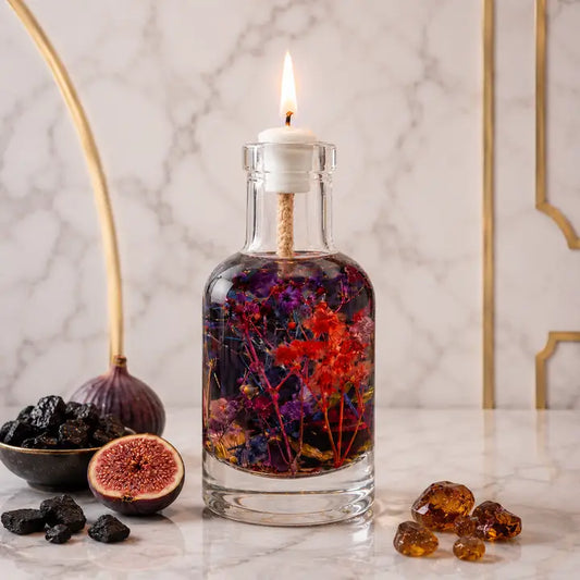 Glass bottle with lit candle inside, filled with dried flowers, on a marble surface with figs and amber beads.