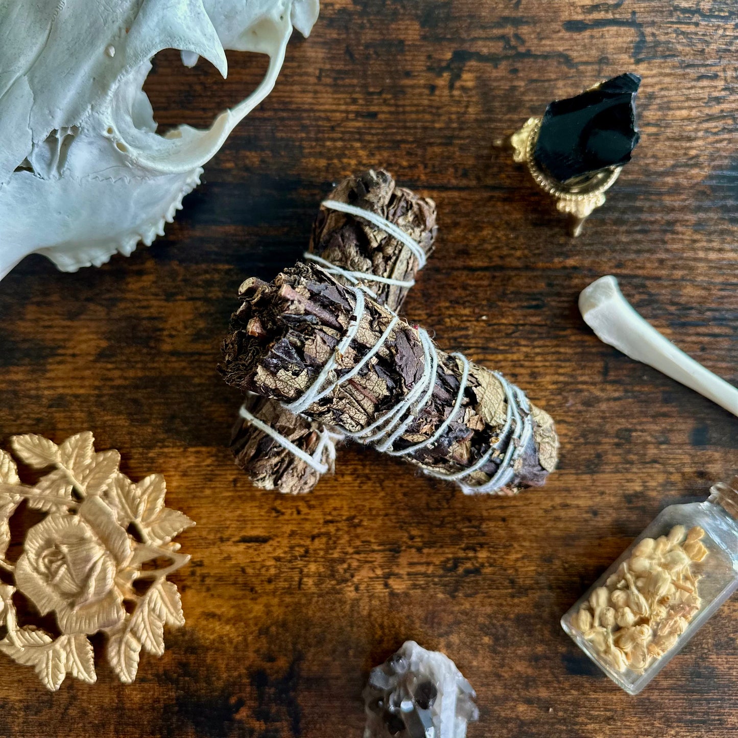 A close-up image of a black sage smudge stick. The bundle features dried black sage leaves tightly wrapped together with natural twine, forming a cylindrical shape. The leaves are a muted green color, with some light brown tones where they have dried. The smudge stick gives off an earthy and cleansing aura, perfect for rituals or purification practices. The texture of the leaves and twine is clearly visible, adding a natural, rustic feel to the image.