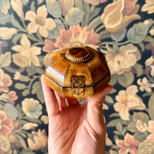 Hand holding a wooden jewelry box against a floral-patterned background