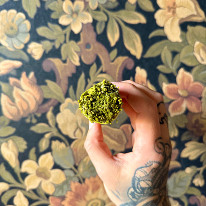 A close-up view of a handcrafted Patchouli Resin Blue Sage Smudge Stick, showcasing its tightly bound, organic blue sage and patchouli resin details against a rustic wallpaper surface.