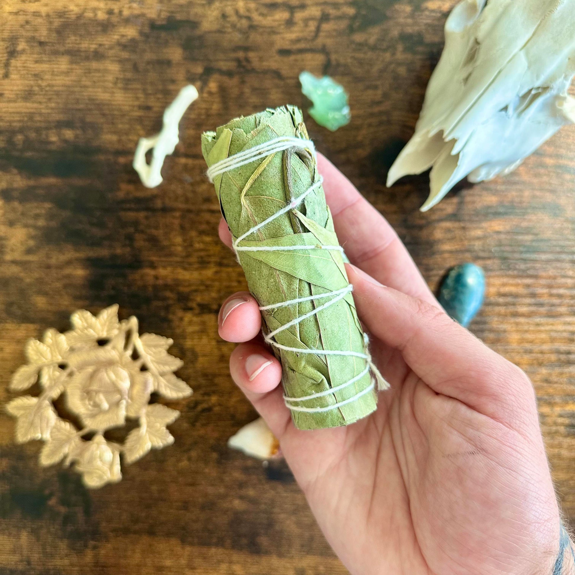 A close-up image of a eucalyptus smudge stick. The bundle features dried eucalyptus leaves tightly wrapped together with natural twine, forming a cylindrical shape. The leaves are a muted green color, with some light brown tones where they have dried. The smudge stick gives off an earthy and cleansing aura, perfect for rituals or purification practices. The texture of the leaves and twine is clearly visible, adding a natural, rustic feel to the image.