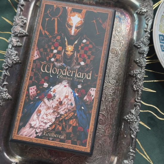 A mesmerizing video showcasing the Wonderland Shadows Tarot Deck. The camera pans across beautifully illustrated cards featuring whimsical characters from Alice in Wonderland, each card adorned with shimmering gold foil edges. Highlights include The Fool (Alice falling into the rabbit hole), The High Priestess (Cheshire Cat), and Justice (White Rabbit). The deck is presented in an elegant, sturdy box with enchanting cover art. 